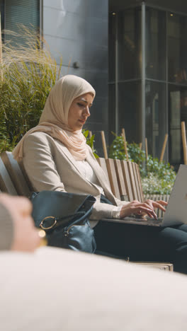 Vertikales-Video-Einer-Muslimischen-Geschäftsfrau,-Die-Draußen-In-Stadtgärten-Sitzt-Und-Am-Laptop-Arbeitet